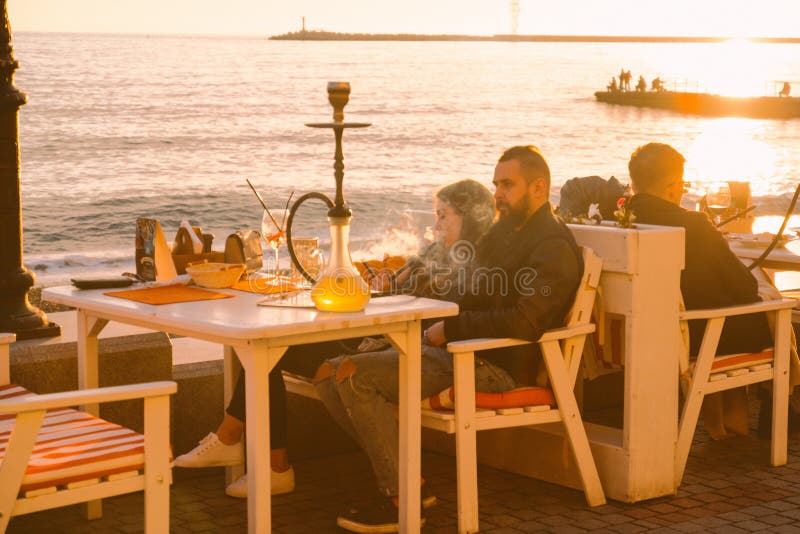 people have dinner  and smoke hookah in a restaurant by the sea at sunset , blurred summer background. people have dinner  and smoke hookah in a restaurant by the sea at sunset , blurred summer background