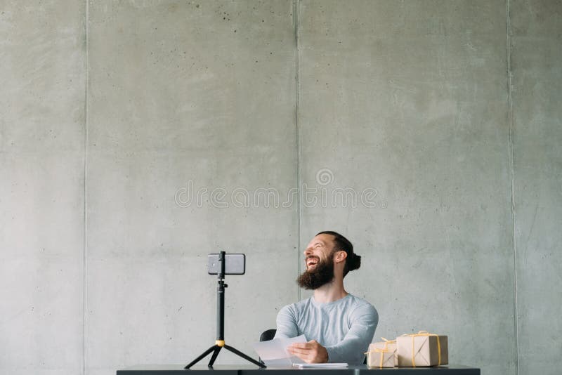 Social video blog. Hipster guy using smartphone on tripod, reading letters, laughing on camera. Copy space. Social video blog. Hipster guy using smartphone on tripod, reading letters, laughing on camera. Copy space.