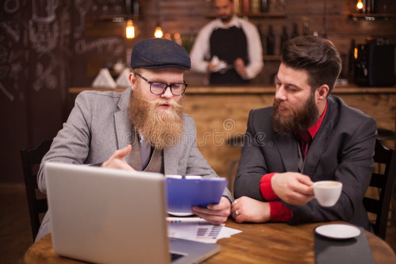 Socio commerciale due che controlla il loro ultimo rapporto durante il tempo della rottura in una caffetteria fotografie stock libere da diritti Socio commerciale due che controlla il loro ultimo rapporto durante il tempo della rottura in una caffetteria fotografie stock libere da diritti