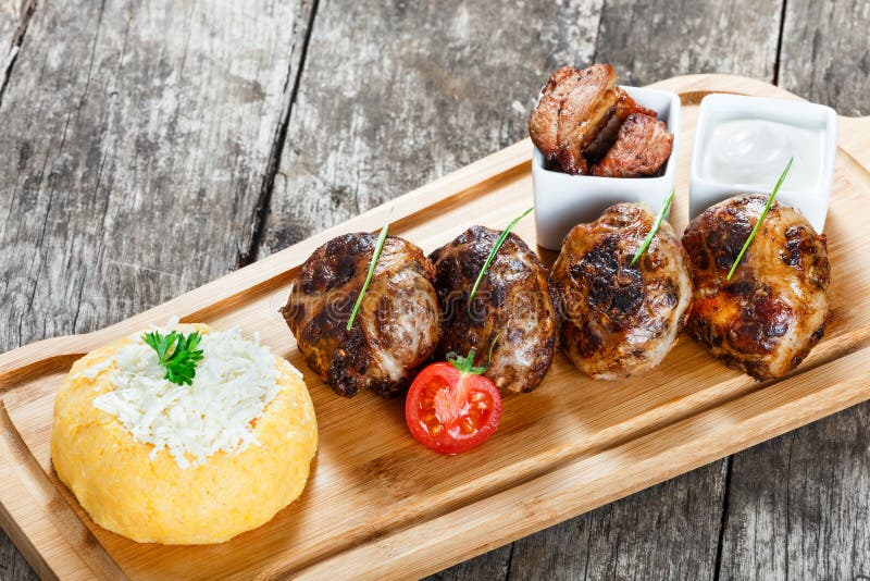 Soczyści wyśmienicie mięśni cutlets, hominy i kukurudzy owsianka polenta z koźlim serem na tnącej desce na drewnianym tle zdjęcia royalty free Soczyści wyśmienicie mięśni cutlets, hominy i kukurudzy owsianka polenta z koźlim serem na tnącej desce na drewnianym tle zdjęcia royalty free
