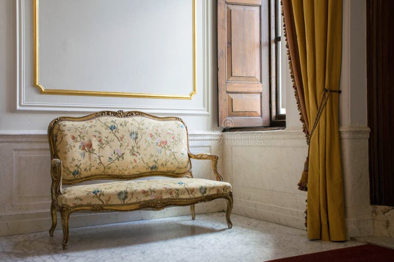 Sofa in stile barocco vicino alla finestra Interni classici con pavimento in marmo e bianco, pareti d'oro Palazzo dei Castelli St