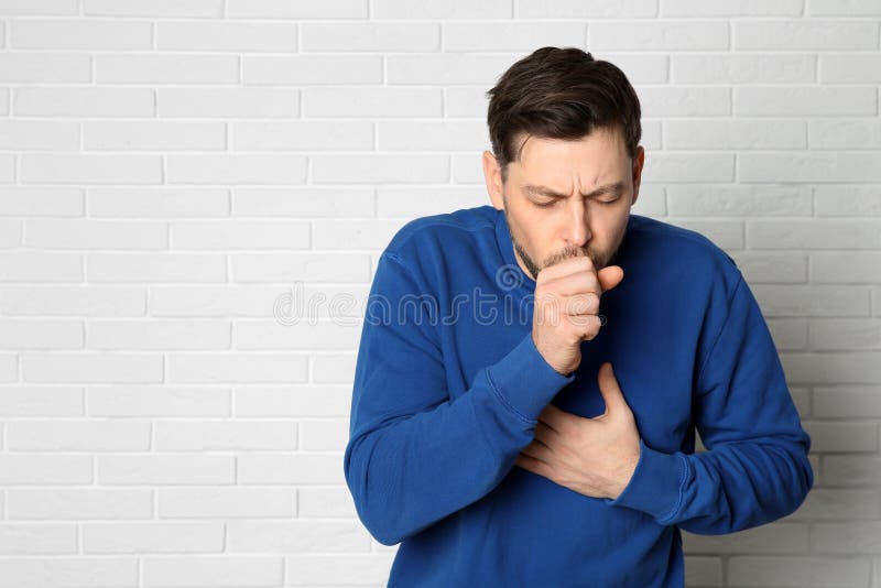 Sofferenza dell'uomo dalla tosse vicino al muro di mattoni