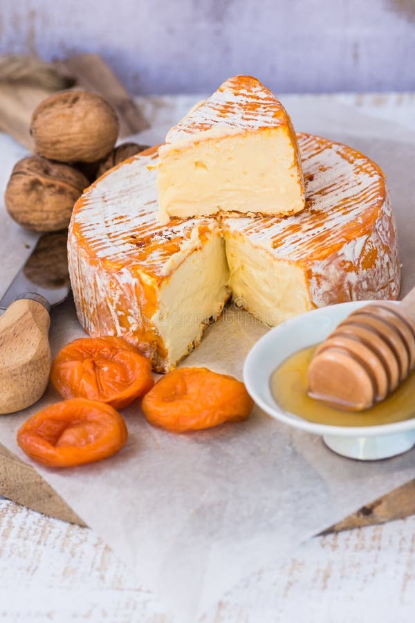 Soft cheese with cut off slice creamy texture, orange rind with mold, French, German, Alps, honey dipper, walnuts, dried apricots royalty free stock photography