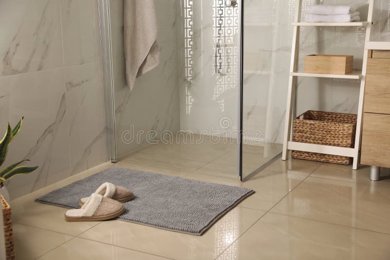 Soft grey bath mat and slippers on floor in bathroom