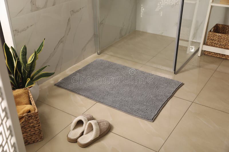 Soft grey bath mat and slippers on floor in bathroom