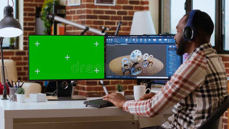 Software developer creates a gear prototype on dual monitors next to chroma key stock photos