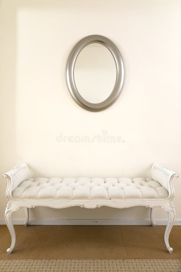 A white luxurious vintage couch underneath a simple mirror. A white luxurious vintage couch underneath a simple mirror.