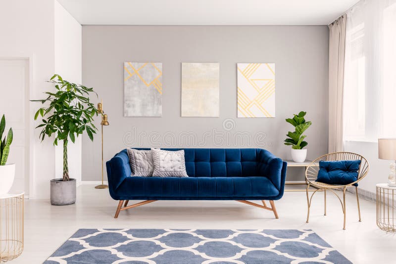 Sofá del azul real con dos almohadas que se colocan en foto real del interior brillante con las plantas frescas, ventana con las