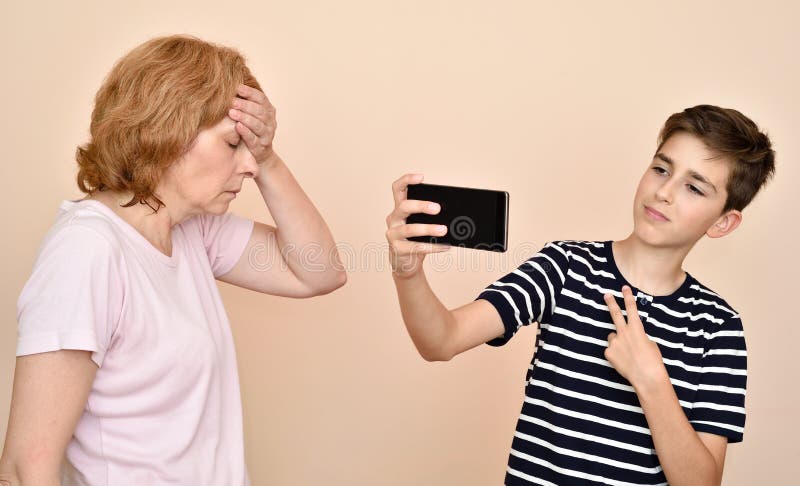 Sohn, der selfie nimmt, während seine Mutter ihren Kopf mit der Hand schlägt stockbild Sohn, der selfie nimmt, während seine Mutter ihren Kopf mit der Hand schlägt stockbild