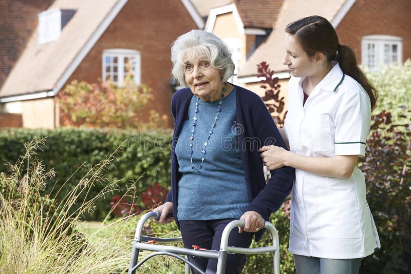 Soignant aidant l'homme supérieur à marcher dans le jardin utilisant le cadre de marche image libre de droits Soignant aidant l'homme supérieur à marcher dans le jardin utilisant le cadre de marche image libre de droits