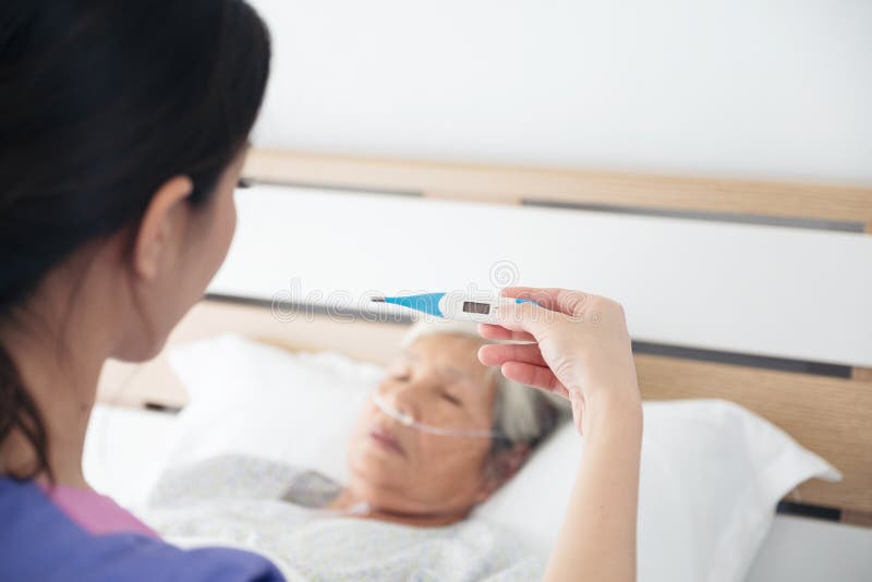 Soignez vérifier la température corporelle patiente en difficulté du ` s - fièvre la vieille Asie images stock Soignez vérifier la température corporelle patiente en difficulté du ` s - fièvre la vieille Asie images stock
