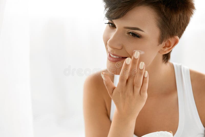 Soins de la peau de beauté Belle femme appliquant la crème de visage cosmétique photographie stock