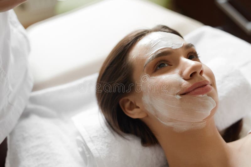 Face Skin Care. Closeup Of Beautiful Healthy Smiling Woman With White Cosmetic Mask On Her Face Relaxing And Enjoying Facial Beauty Treatment At Day Spa Salon Indoors. High Resolution Image. Face Skin Care. Closeup Of Beautiful Healthy Smiling Woman With White Cosmetic Mask On Her Face Relaxing And Enjoying Facial Beauty Treatment At Day Spa Salon Indoors. High Resolution Image