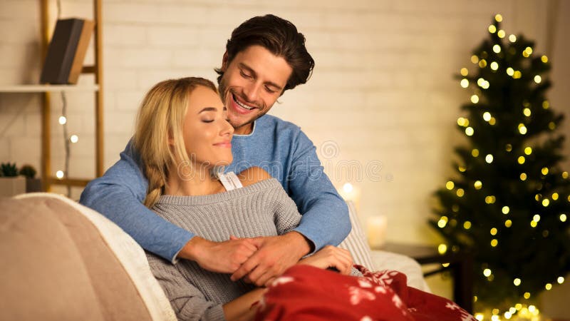 Soirée de Noël cosy Un couple aimant embrasser près de l'arbre de Noël. Soirée de Noël cosy Un couple aimant embrasser près du sapin de Noël, reposant sur un canapé