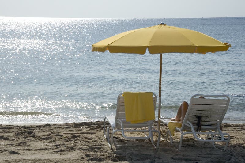 A yellow beach umbrella provides shade for a young woman. A yellow beach umbrella provides shade for a young woman.