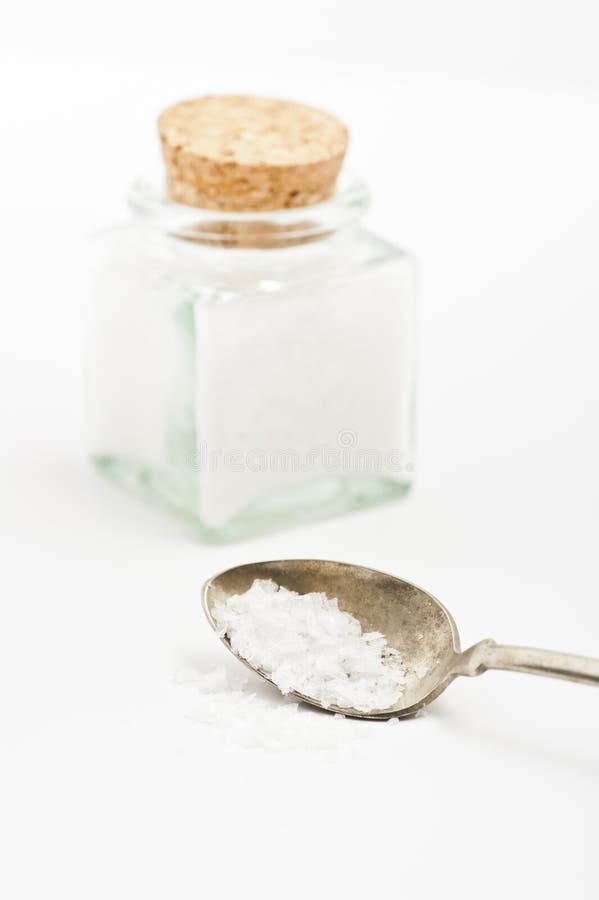 Spoon with salt and jar containing salt. Spoon with salt and jar containing salt