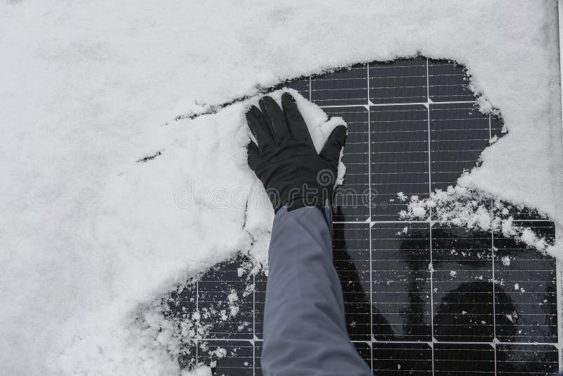 Solar energy in winter time.Getting electricity with solar panels in winter.Hands in black gloves clear snow from solar