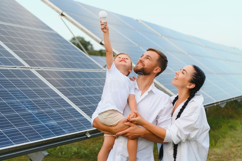 Solarenergiekonzept. eine junge glückliche Familie steht in der Nähe von Solarzellen und hält eine elektrische Glühbirne. stockfoto