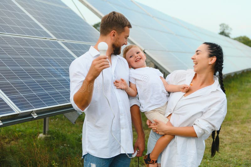 Solarenergiekonzept. eine junge glückliche Familie steht in der Nähe von Solarzellen und hält eine elektrische Glühbirne. stockfoto