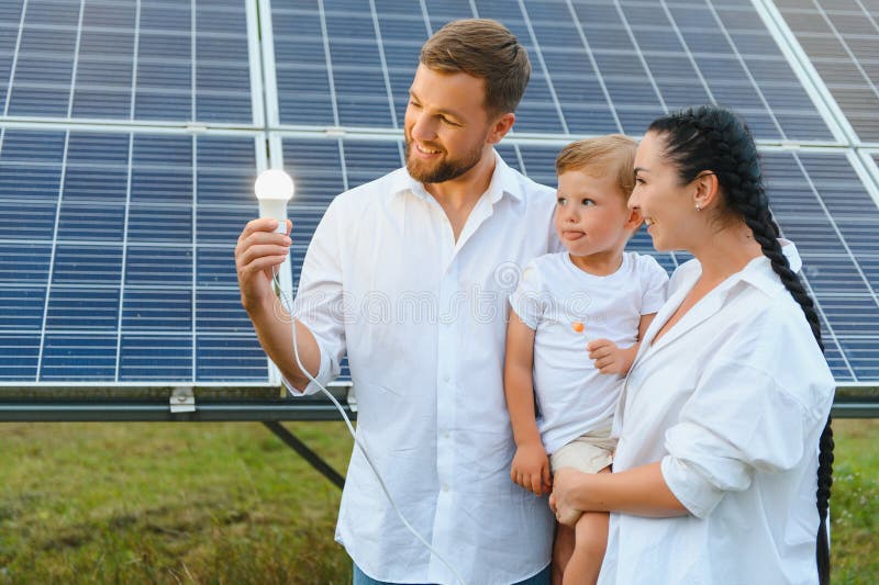 Solarenergiekonzept. eine junge glückliche Familie steht in der Nähe von Solarzellen und hält eine elektrische Glühbirne. stockfotografie
