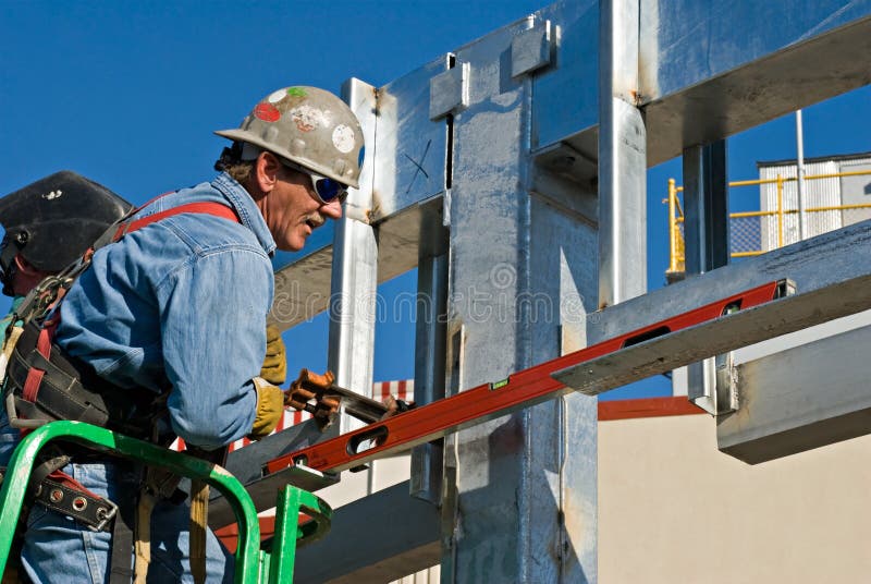 Construction welder tightening clamp to level metal supports. Construction welder tightening clamp to level metal supports.