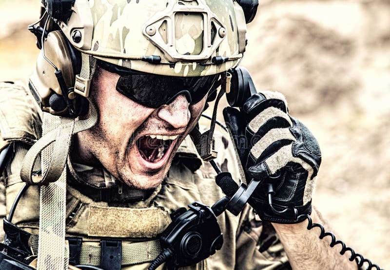 Special forces soldier, military communications operator or maintainer in helmet and glasses, screaming in radio during battle in desert. Calling up reinforcements, reporting situation on battlefield. Special forces soldier, military communications operator or maintainer in helmet and glasses, screaming in radio during battle in desert. Calling up reinforcements, reporting situation on battlefield