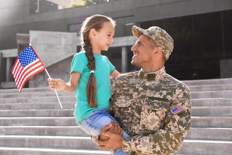 Soldat und seine kleine Tochter mit amerikanischer Flagge im Freien. Tag der Veteranen in Klausen stockfoto