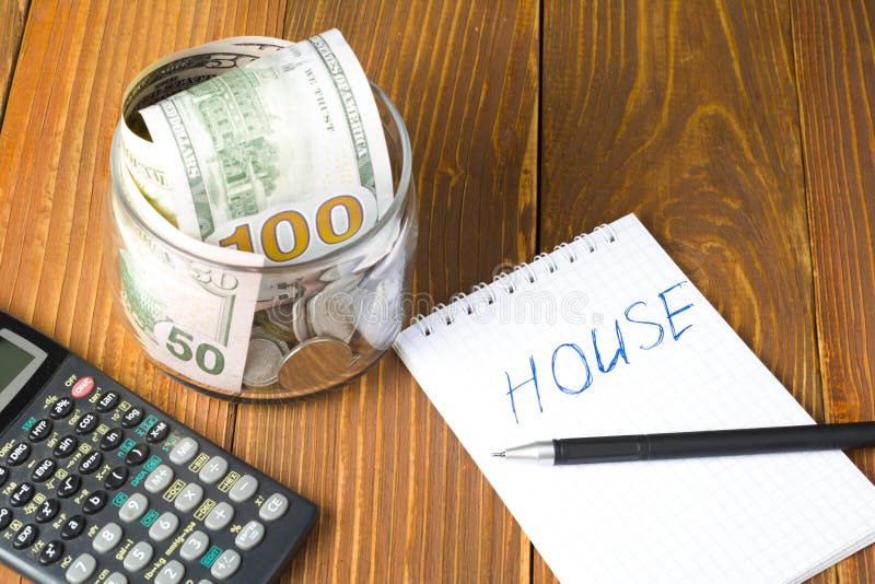 Soldi in barattolo, calcolatore e blocco note di vetro con la parola CASA a fondo di legno Risparmio e concetto di finanza fotografia stock libera da diritti Soldi in barattolo, calcolatore e blocco note di vetro con la parola CASA a fondo di legno Risparmio e concetto di finanza fotografia stock libera da diritti