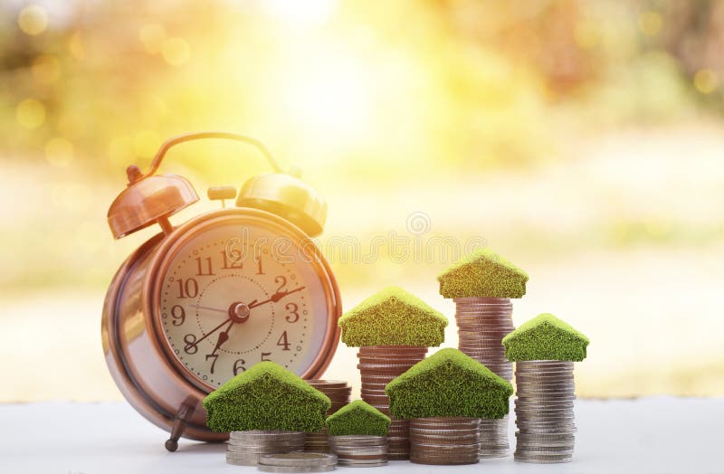 Soldi sopra impilati delle monete per conservare per la casa, il piccolo albero e la casa sul mucchio con la sveglia sulla tavola immagine stock Soldi sopra impilati delle monete per conservare per la casa, il piccolo albero e la casa sul mucchio con la sveglia sulla tavola immagine stock