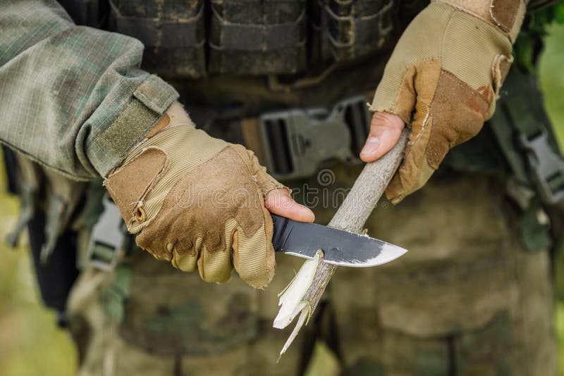 Giovane soldato con un coltello tagliare un bastone di legno.