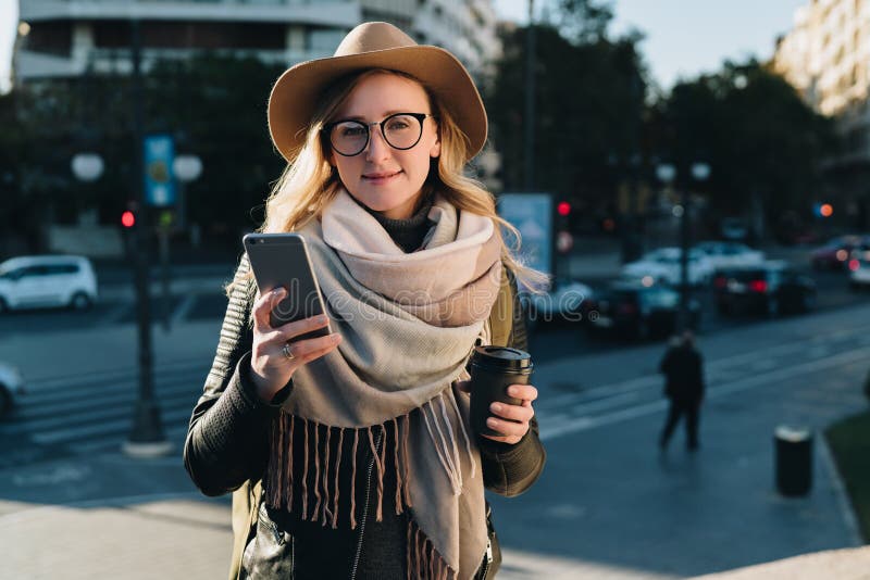 solig höstdag Den unga attraktiva kvinnan reser i hatt, och glasögon står på stadsgatan, använder smartphonen royaltyfria foton solig höstdag Den unga attraktiva kvinnan reser i hatt, och glasögon står på stadsgatan, använder smartphonen royaltyfria foton