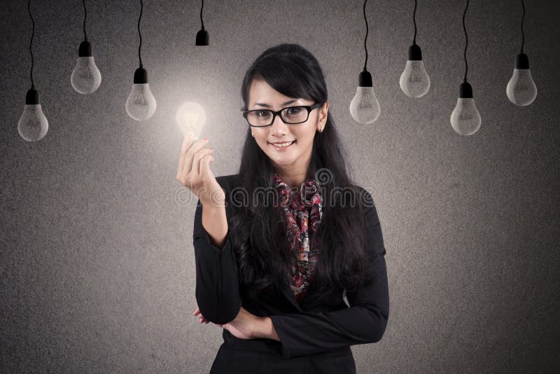 Beautiful Asian Businesswoman with glasses holds bright lightbulb. Beautiful Asian Businesswoman with glasses holds bright lightbulb