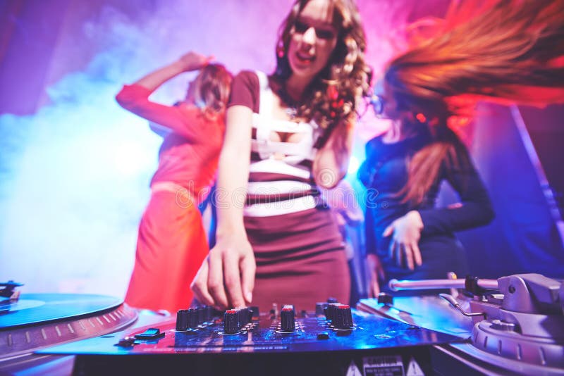 Girl adjusting deejay equipment with dancing friends behind. Girl adjusting deejay equipment with dancing friends behind