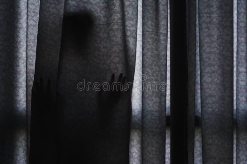 Sombra do ` s da mulher que está escondendo atrás da cortina