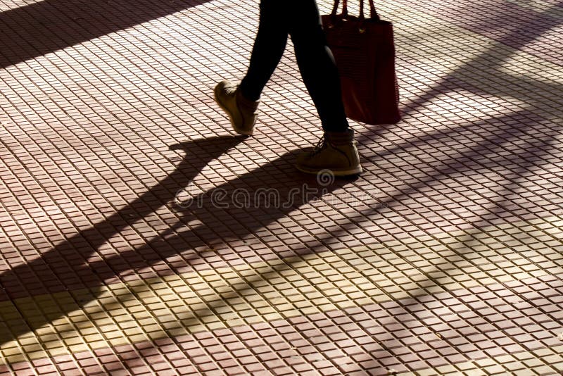 Sombra obscura da silhueta dos pés de uma pessoa que leva um saco ao andar no passeio telhado da rua