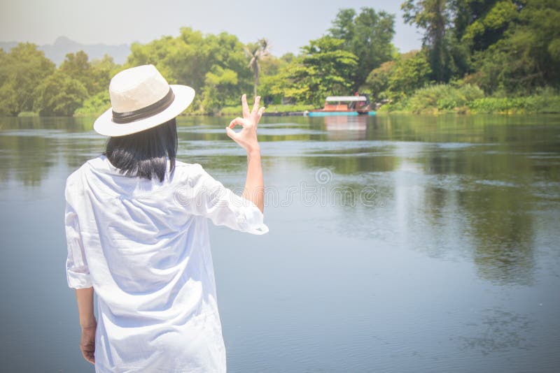 Sombrero del desgaste de mujer y la camisa blanca con la situaci?n en el puente de madera, ella que mira adelante al r?o con hace fotos de archivo libres de regalías Sombrero del desgaste de mujer y la camisa blanca con la situaci?n en el puente de madera, ella que mira adelante al r?o con hace fotos de archivo libres de regalías