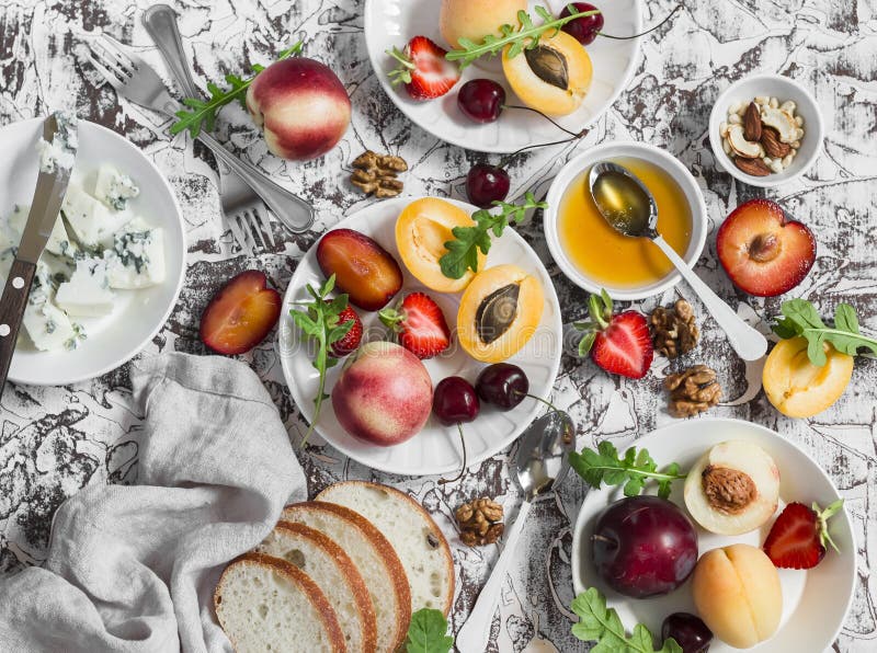 Sommar bär frukt - aprikors, persikor, plommoner, körsbär, jordgubbar och ädelost, honung, valnötter på en ljus stenbakgrund läka arkivbilder Sommar bär frukt - aprikors, persikor, plommoner, körsbär, jordgubbar och ädelost, honung, valnötter på en ljus stenbakgrund läka arkivbilder