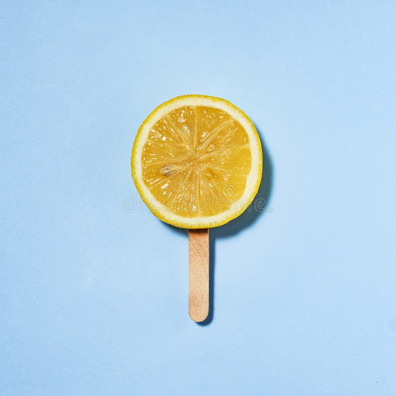 Sommarcitron på en pinne i stället för glass en bit saftig citron på blå bakgrund. Sommarcitron på en pinne i stället för glass en bit saftig citron på en blå, minimal kreativ idé