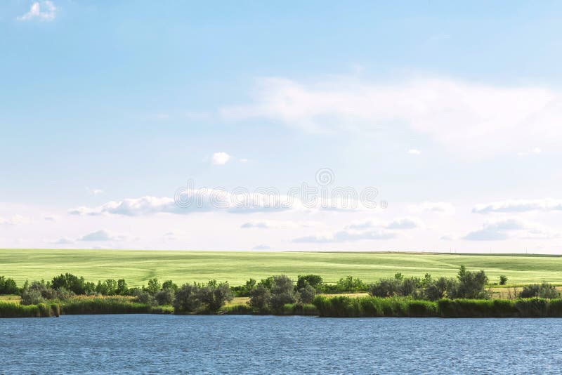 Sommarlandskap med en härlig blå sjö och gröna fält mot en blå himmel Fotvandra och att fiska på dammet Resa till floden royaltyfri foto Sommarlandskap med en härlig blå sjö och gröna fält mot en blå himmel Fotvandra och att fiska på dammet Resa till floden royaltyfri foto