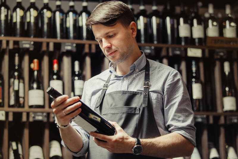 Sommelier joven que sostiene la botella de vino rojo en sótano imágenes de archivo libres de regalías Sommelier joven que sostiene la botella de vino rojo en sótano imágenes de archivo libres de regalías