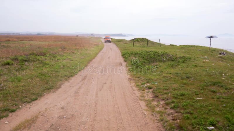 Sommer 2019 - Primorsky Krai, Russland - Orange Expedition Minibus Sable auf einer staubigen Straße zwischen Grünflächen