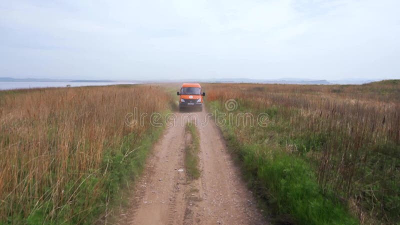 Sommer 2019 - Primorsky Krai, Russland - Orange Expedition Minibus Sable auf einer staubigen Straße zwischen Grünflächen