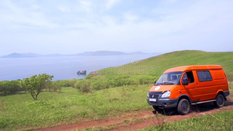 Sommer 2019 - Primorsky Krai, Russland - Orange Expedition Minibus Sable auf einer staubigen Straße zwischen Grünflächen