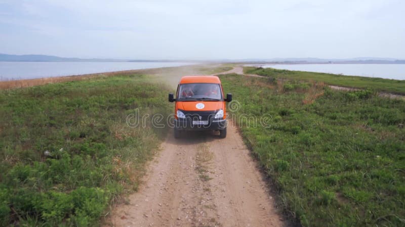 Sommer 2019 - Primorsky Krai, Russland - Orange Expedition Minibus Sable auf einer staubigen Straße zwischen Grünflächen