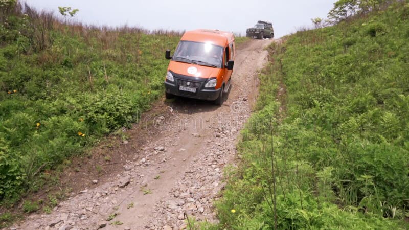 Sommer 2019 - Primorsky Krai, Russland - Orange Expedition Minibus Sable auf einer staubigen Straße zwischen Grünflächen