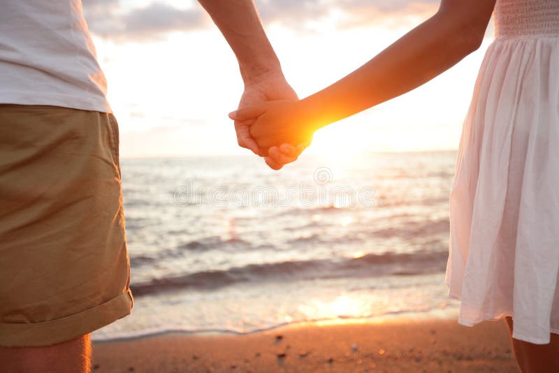 Sommerpaare, die Hände am Sonnenuntergang auf Strand halten