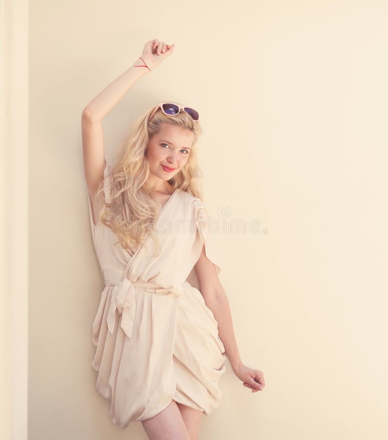 Summer portrait of young beautiful blond woman in white dress posing near the wall and have fun. Summer portrait of young beautiful blond woman in white dress posing near the wall and have fun