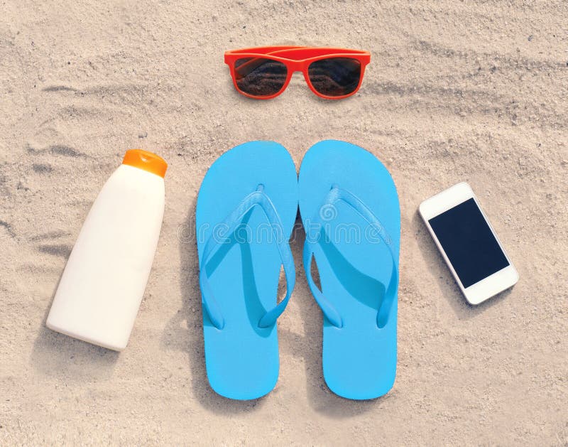 Summer accessories red sunglasses and flip flops with sunscreen bottle smartphone lie on sand beach. Summer accessories red sunglasses and flip flops with sunscreen bottle smartphone lie on sand beach