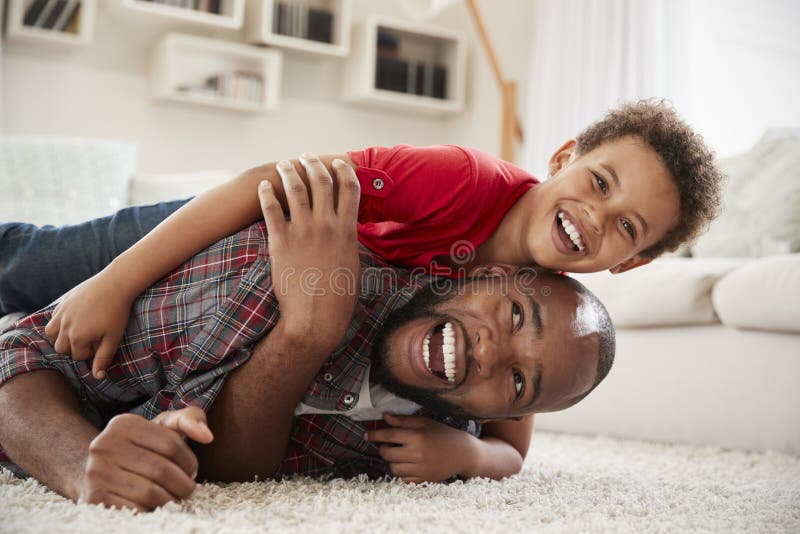 Son Climbs On Fathers Back As They Play Game In Lounge Together royalty free stock images Son Climbs On Fathers Back As They Play Game In Lounge Together royalty free stock images