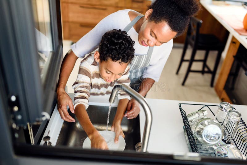 Son is helping mother in the Kitchen, Washing Dishes. African American family.Single mother. Household chores for kids. Son is helping mother in the Kitchen, Washing Dishes. African American family.Single mother. Household chores for kids.